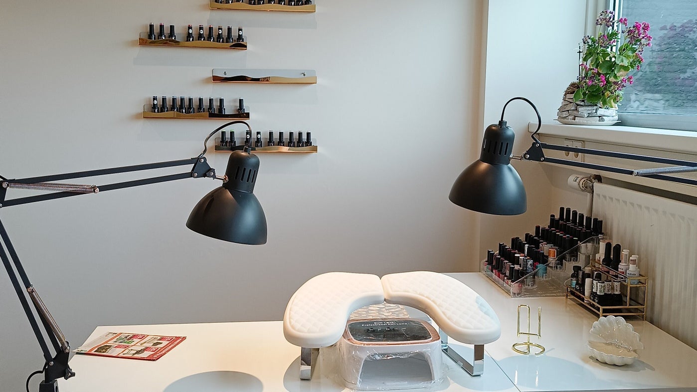De witte werktafel met twee zwarte lampen, de nagellamp en een wand vol kleuren gellak
