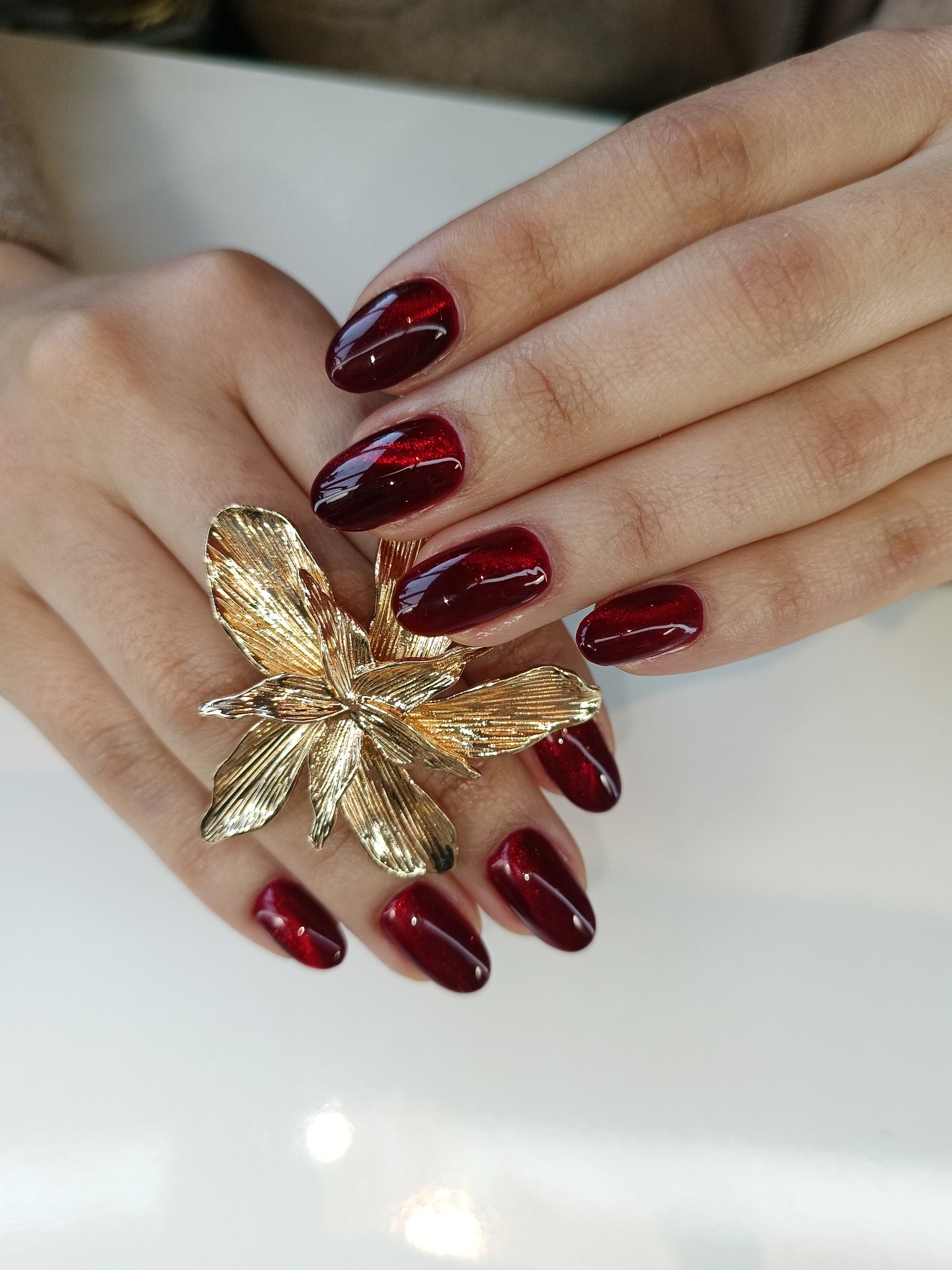 Donkerrode cat eye nagels naast een gouden bloem